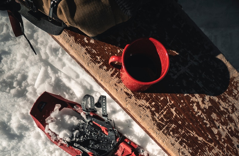coffee cup, backpack, snowshoe and bench on snow