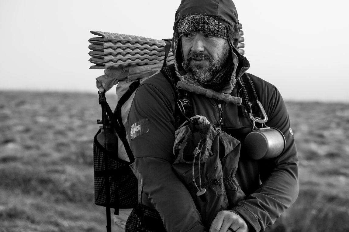 A close up shot of Greg Mills on the tundra near Kotzebue.  Mills is wearing his backpack and looking off in the distance.  