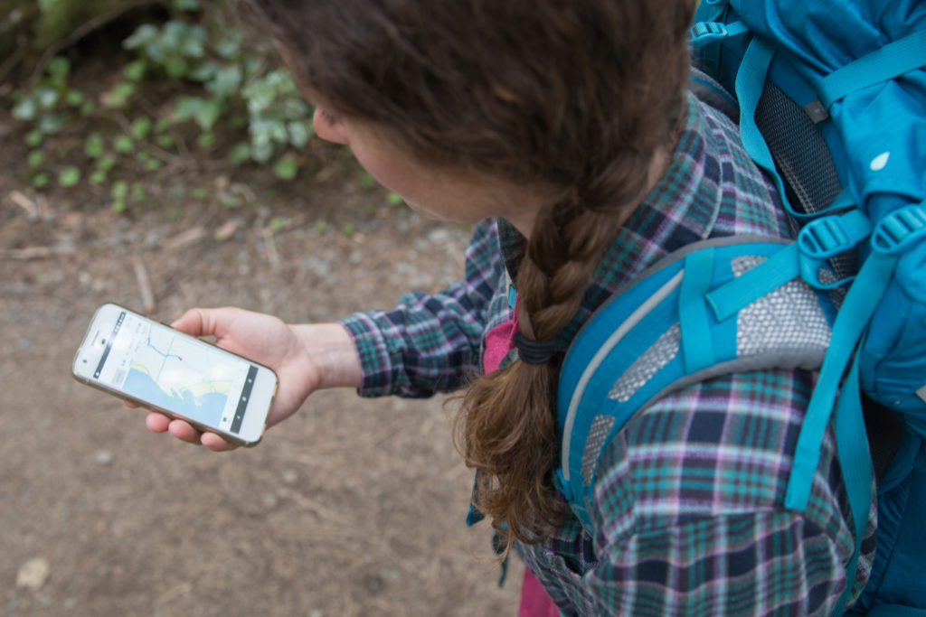 A woman backpacker holding and looking at a phone with a topographical map on the screen.  