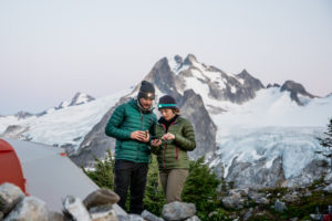 A man and woman standing on top of a mountian looking at a cell phone for navigation.