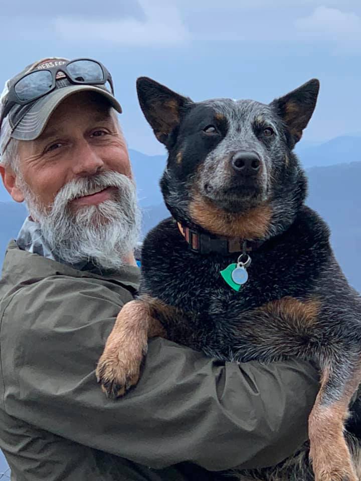 A man holding a cattle dog and smiling. 