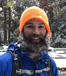 the host of the podcast Andrew Baldwin wearing an orange hat and blue jacket with a frosty beard, smiling