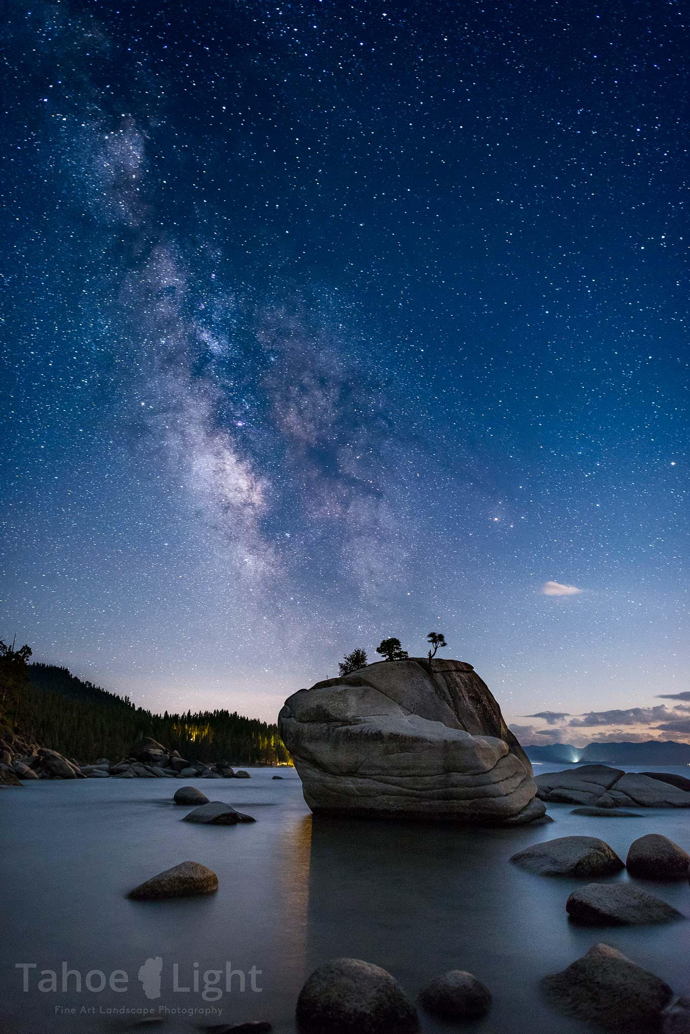 A night sky with stars and the Milky Way in the distance and a rock island in the foreground.  