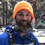 the host of the podcast Andrew Baldwin wearing an orange hat and blue jacket with a frosty beard, smiling