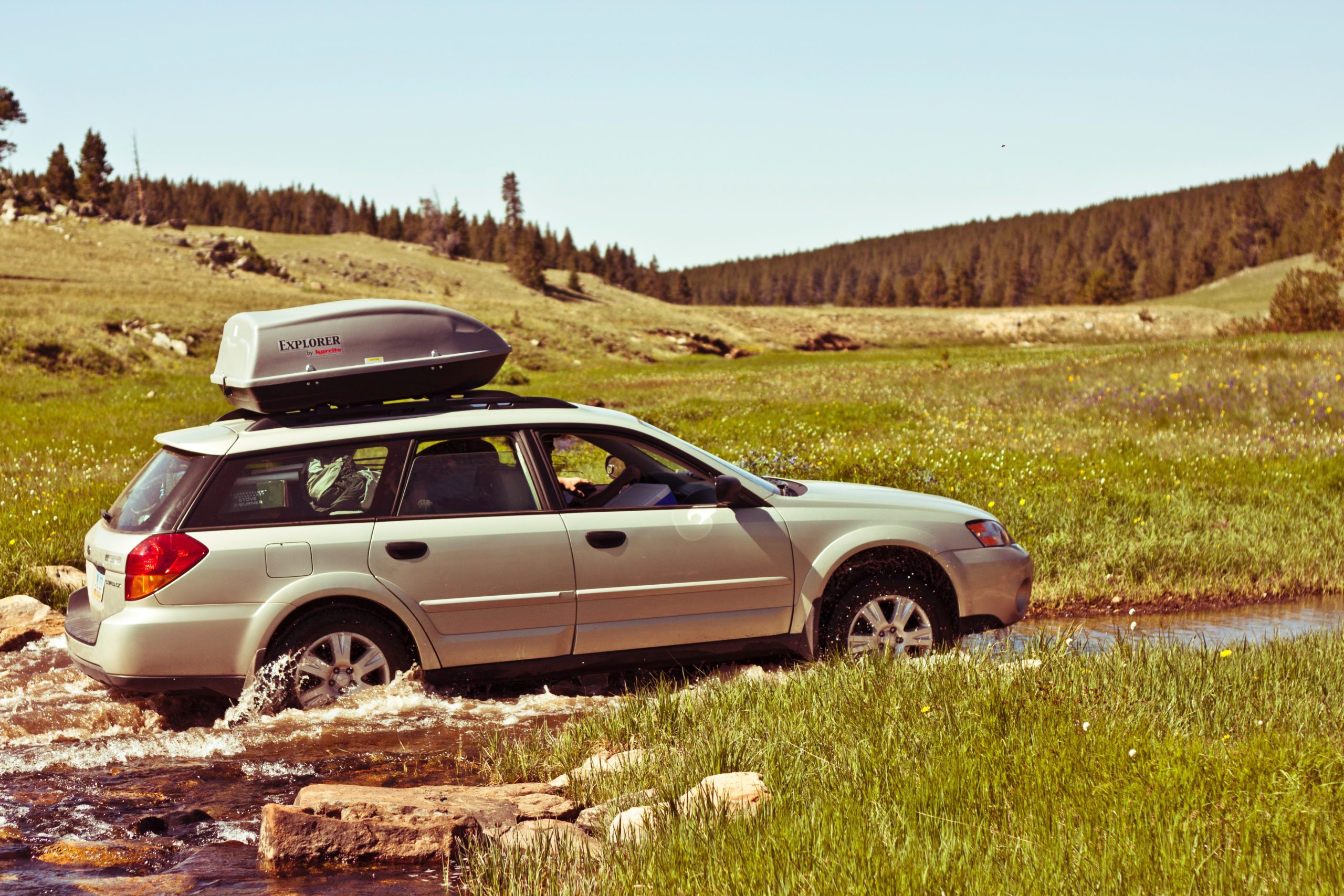 A Subaru Outback negotiates a stream running through a field.