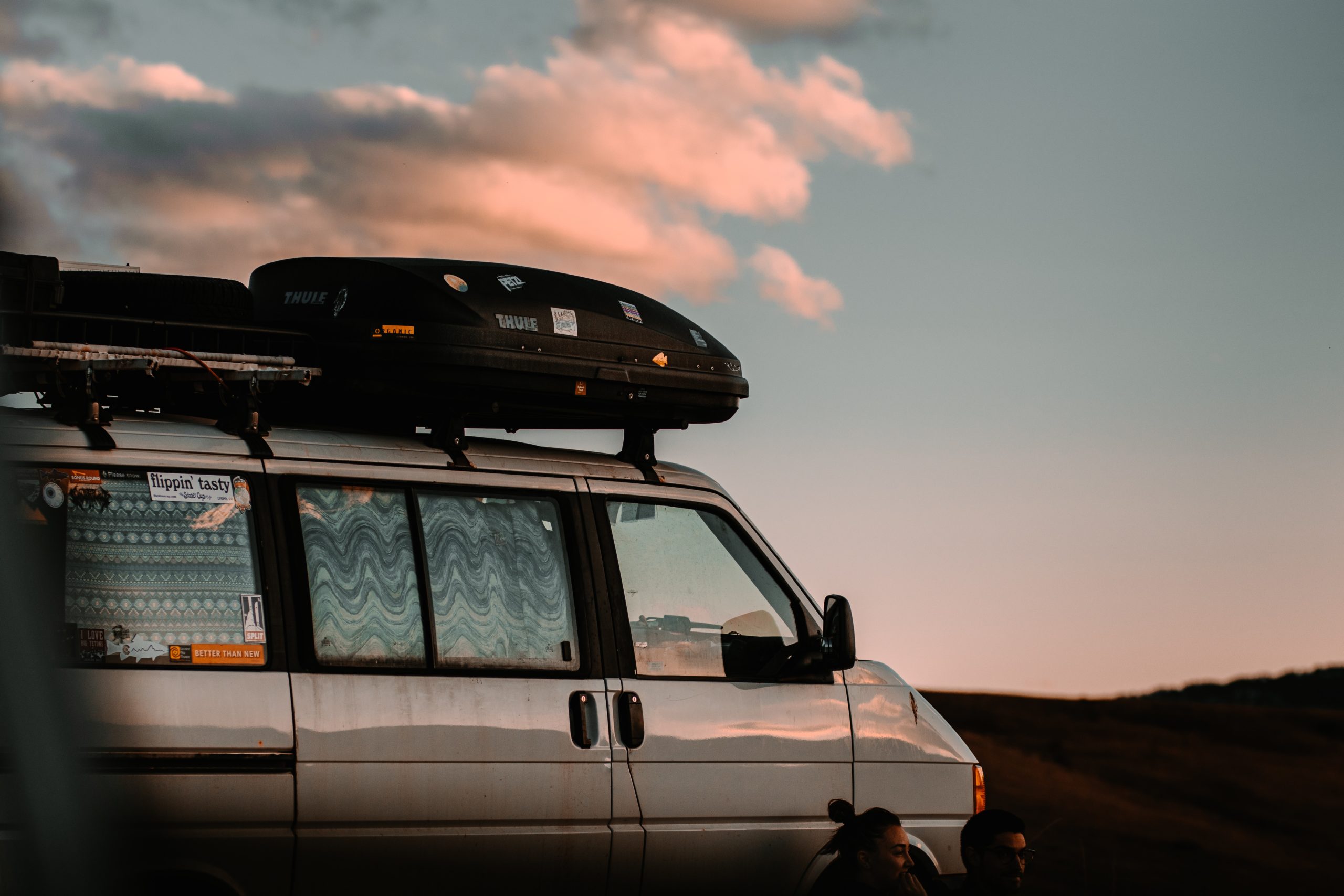 Two people sit outside a van parked at sunset. 