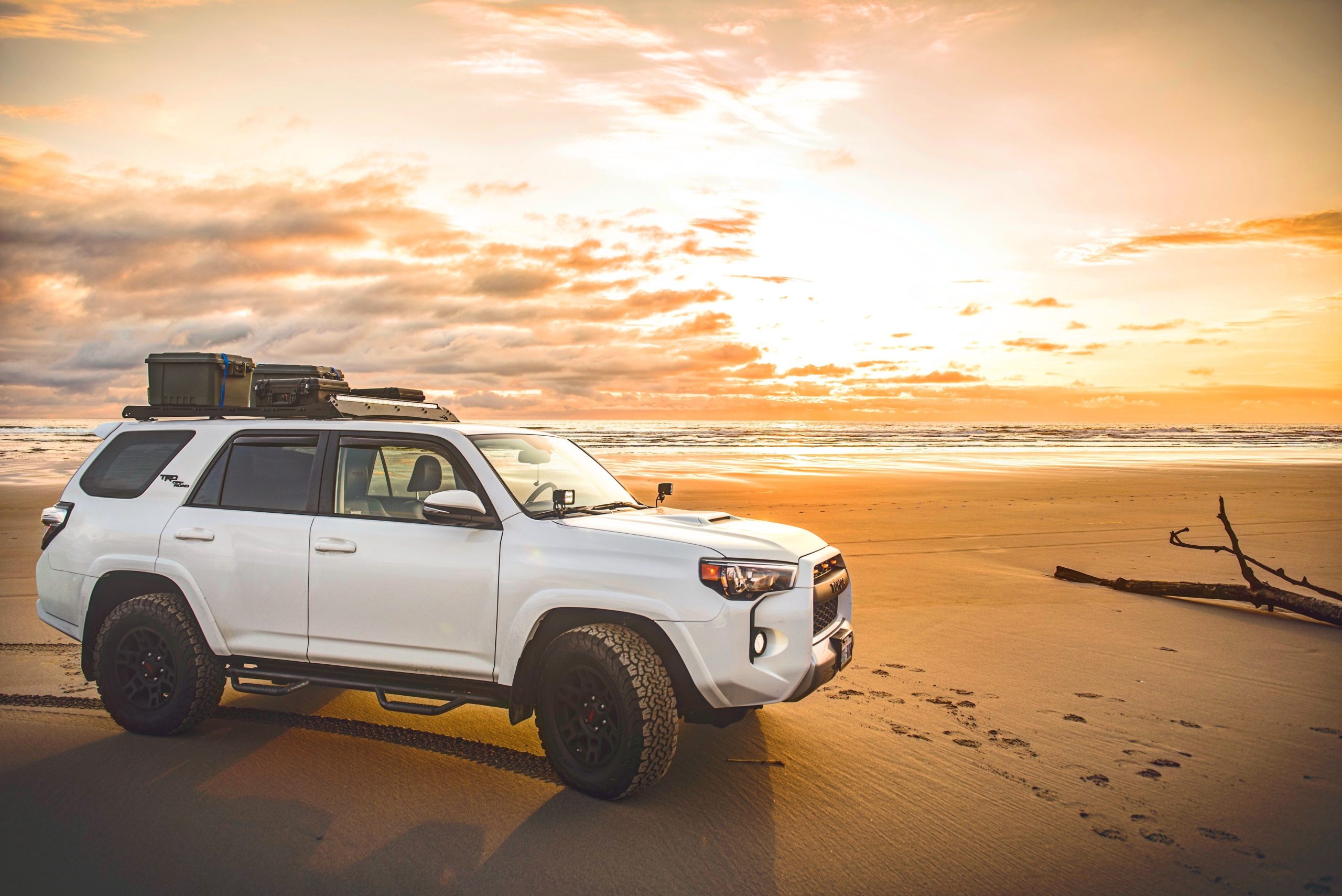 An SUV with a roof rack is parked on a beach at sunset.