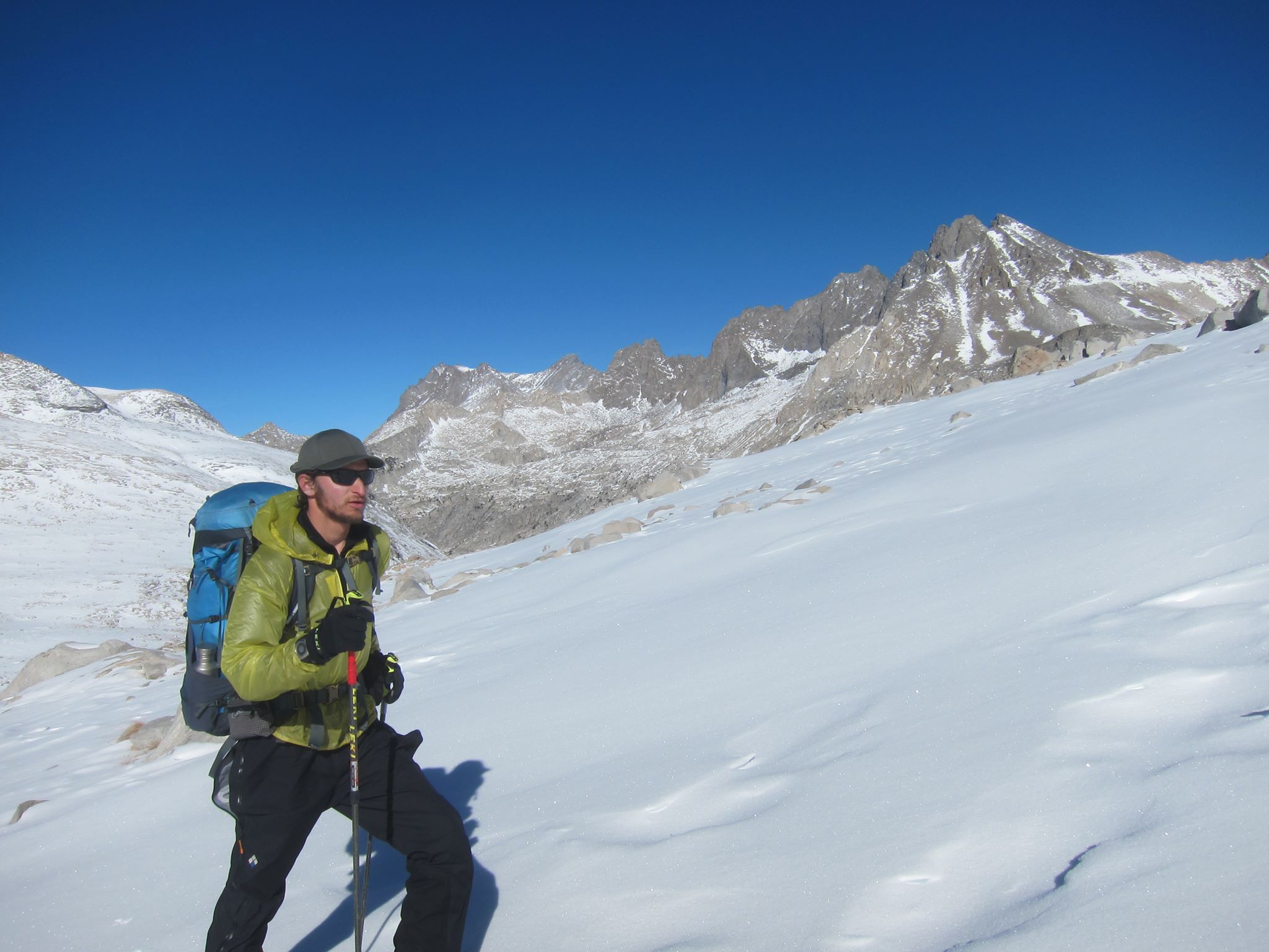 Justin Lichter backcountry skis across a wind-swept snowfield. Barren, rocky peaks jut out of the snow behind him.