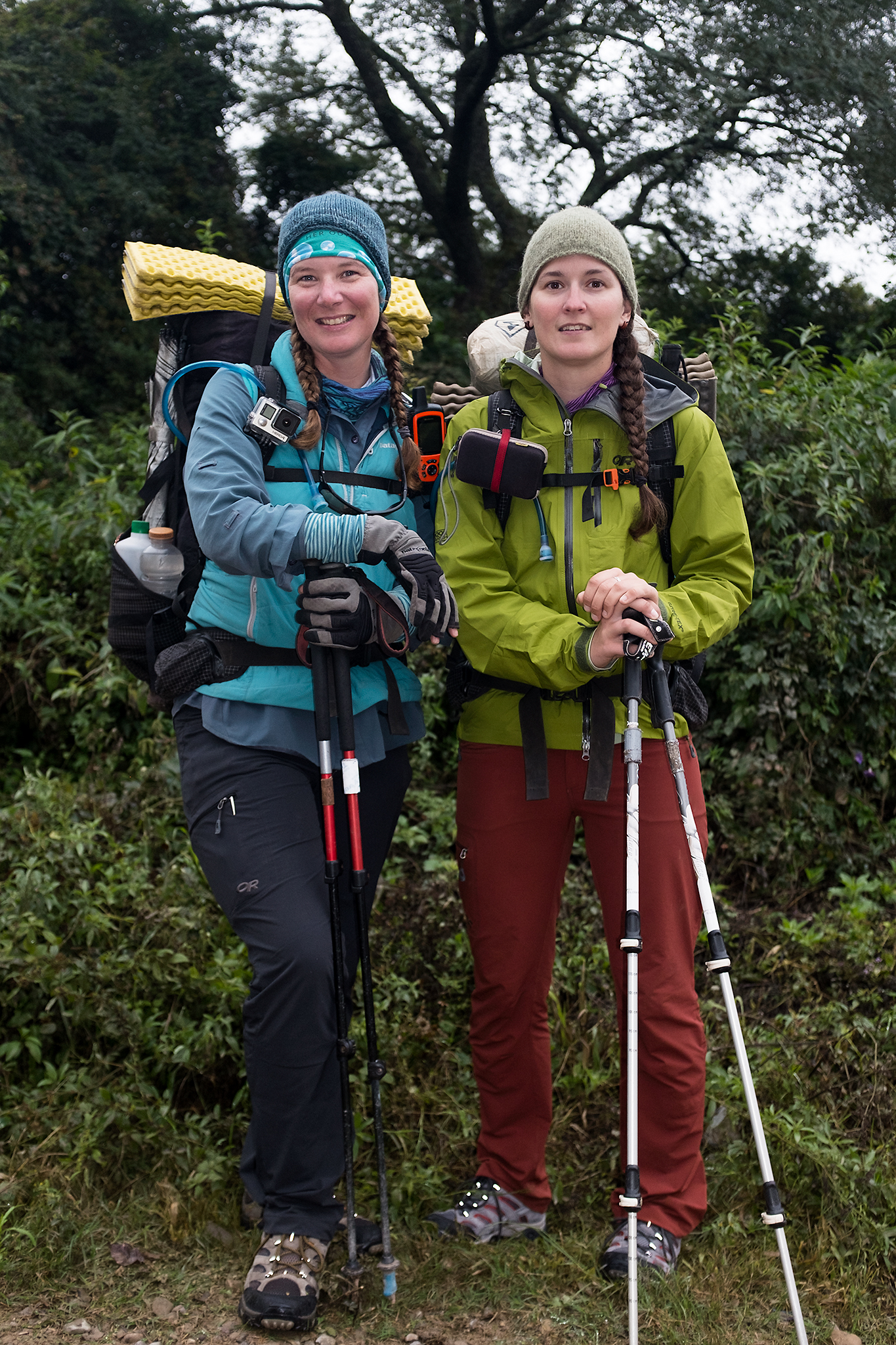 Fidgit (left) and Neon (right) smile for the camera with their backpacking gear. They're standing in front of a forest. 