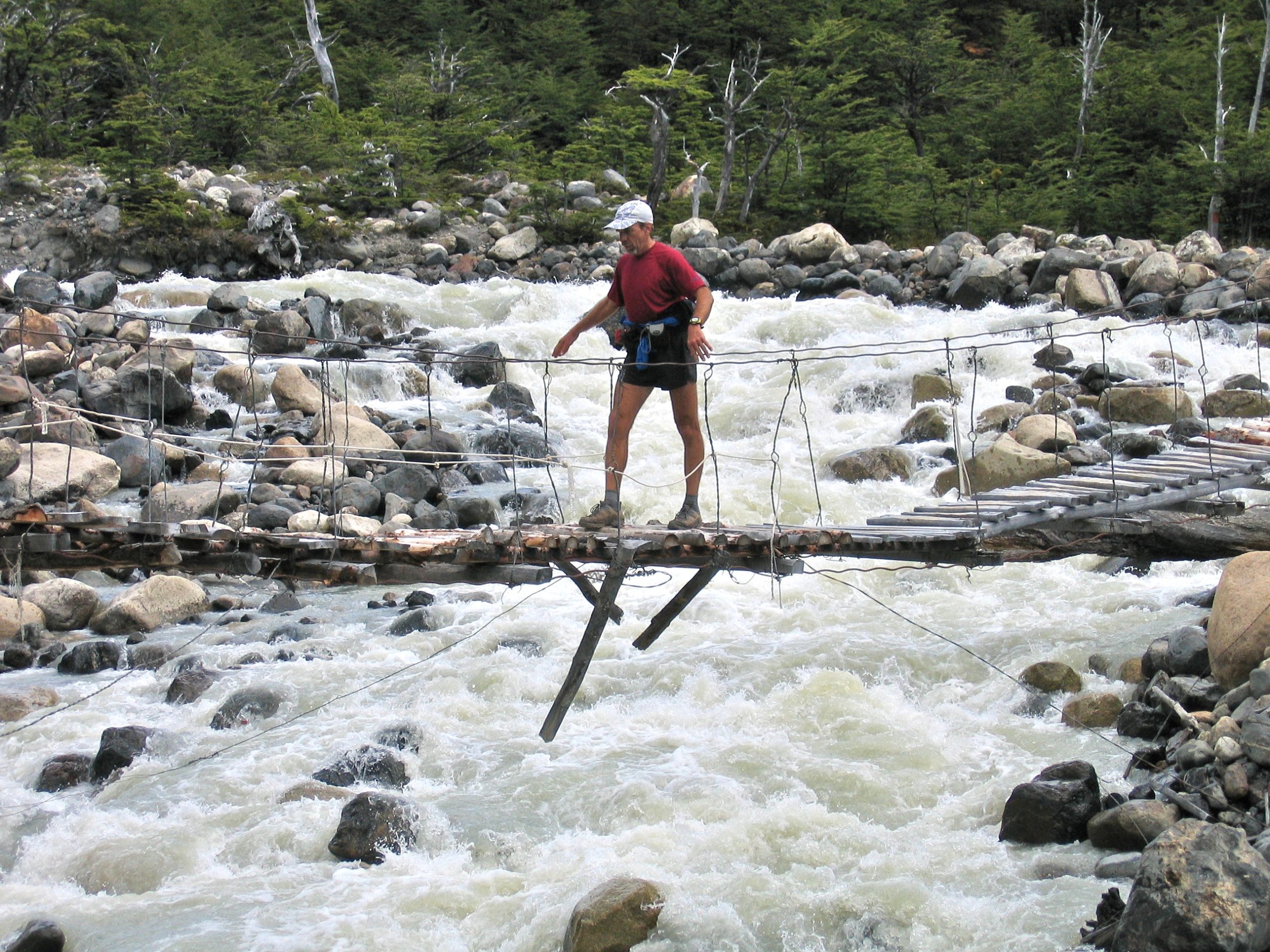 Buzz walks across a log suspension bridge over a raging river.