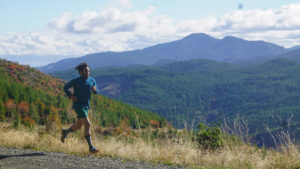 a runner passes by mountains with a touch of fall color.