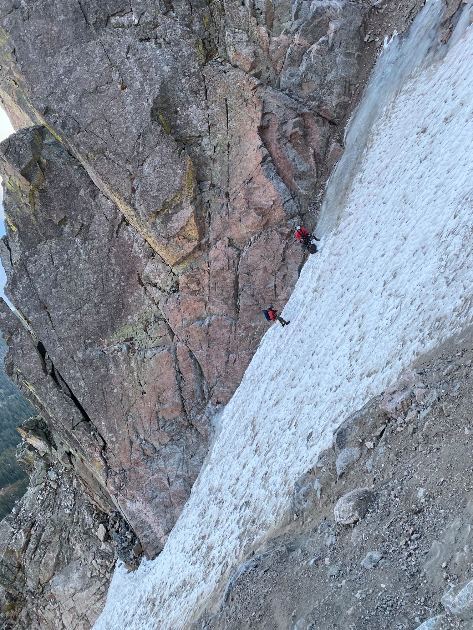 Two people rappel down a steep snow field.