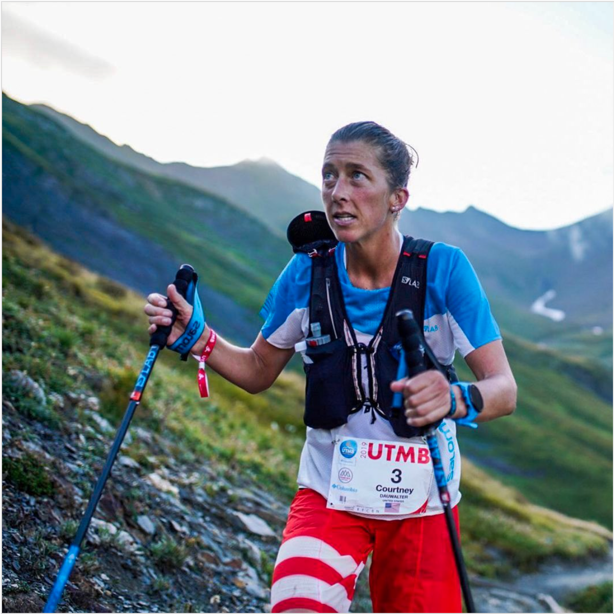 Courtney looks up while trekking up a mountain during UTMB. She's holding her hiking poles in either hand and wearing a hydration vest.