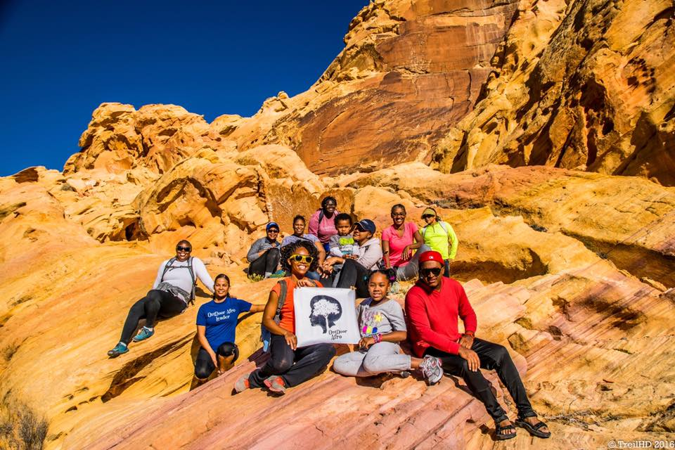 A group of hikers sit and smile for the camera on a rocky desert feature.