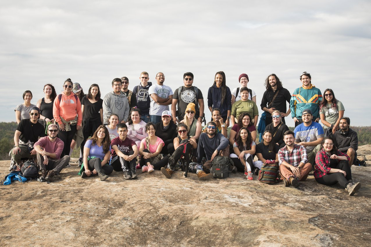 A large group of hikers pose for the camera on top of a rocky outcropping.