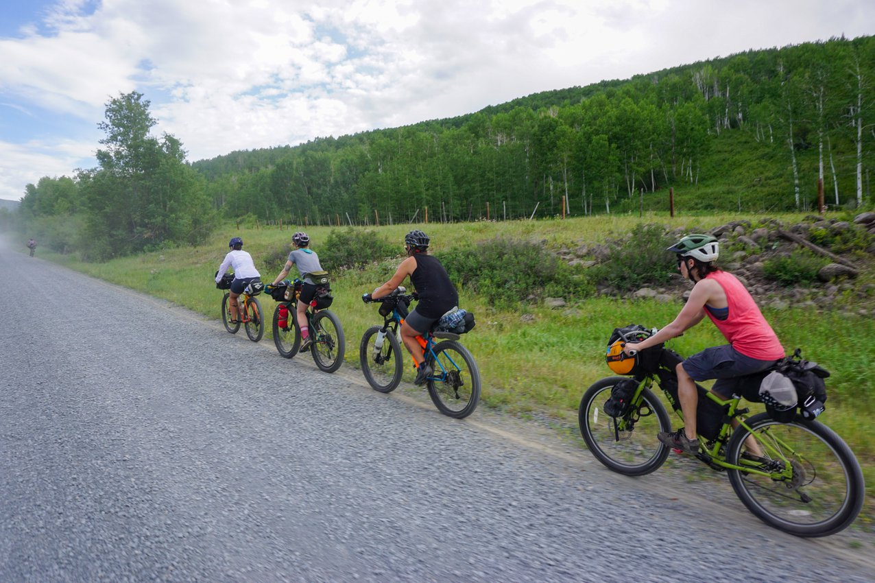 Four bikepackers ride in a single file down a gravel road.