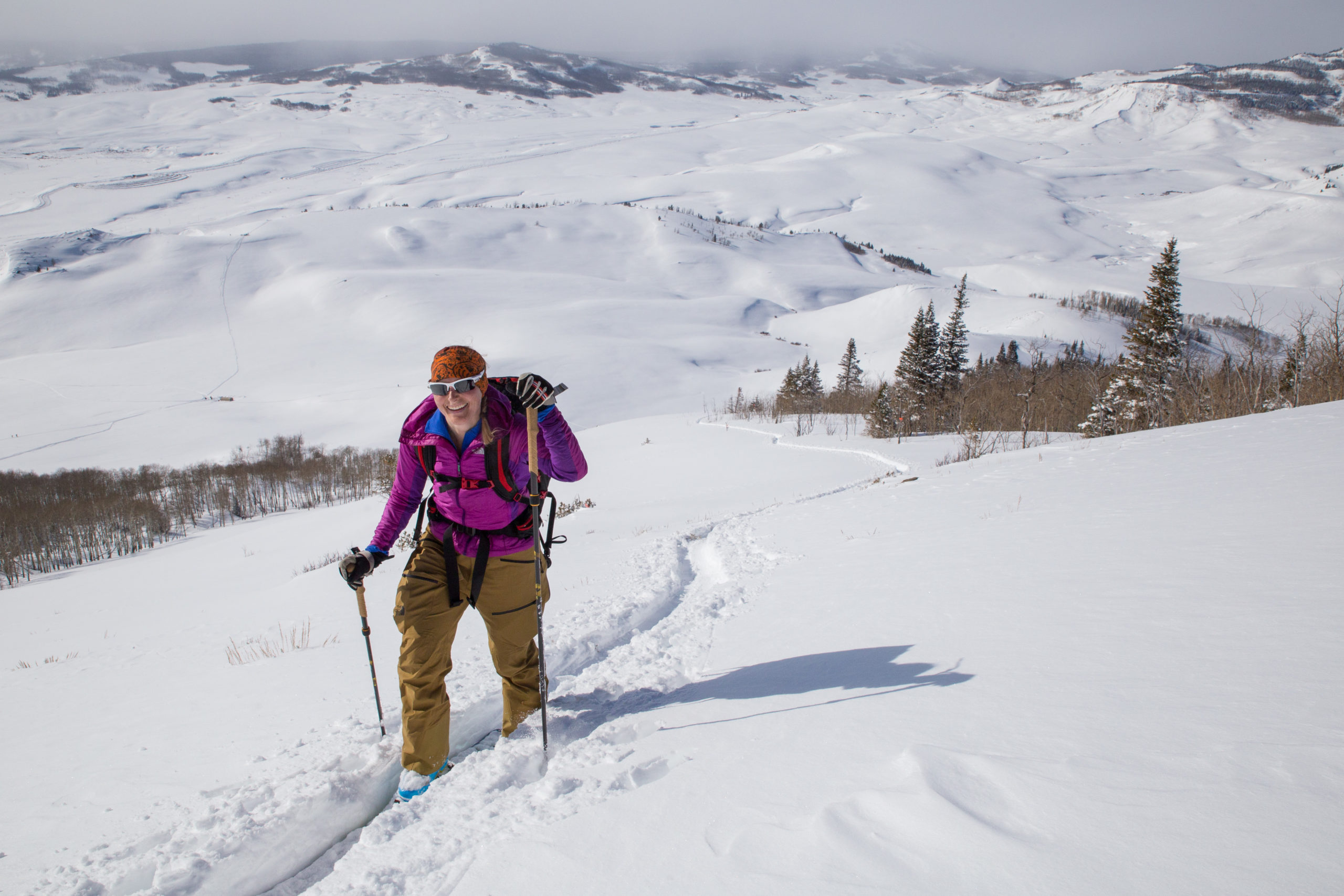 A backcountry skier skins up a track. Snow-covered plains sprawl out behind her.