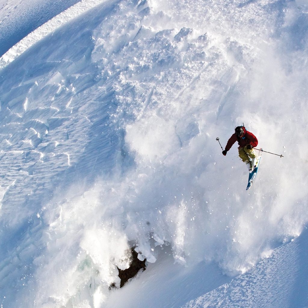 A skier flies through the air as snow shoots down the mountain below.