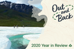 Three hikers gross a snow field with a river in the foreground and mountains in the distance. "Out and Back: 2020 Year in Review" is overlayed on top.
