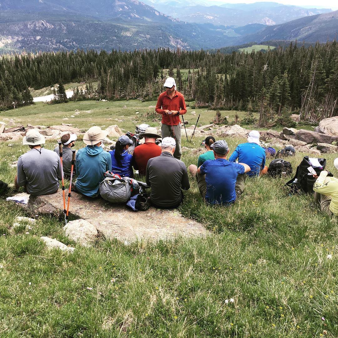 Andrew Skurka teaches backcountry navigation with map and compass in Rocky Mountain national Park. He stands in a meadow facing a group of people sitting on the ground.