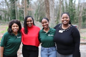Angelou, two GYF interns, and another employee smile for the camera while standing in a line with their arms around each other's shoulders.