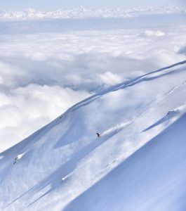 Smithwick skis down a giant Himalayan slope with clouds and tall snowcapped peaks in the distance.