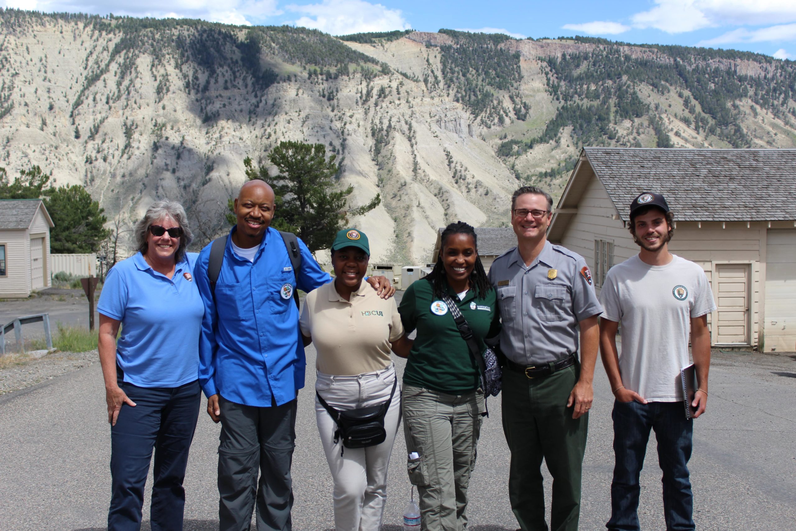Angelou poses for the camera with five other NPS people. They are smiling and standing in a line in front of big rock walls in the background.