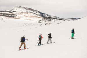 Four backcountry skiers walk up a snowy mountain.