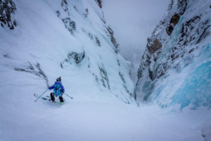A skier stands at the top of an icy couloir.