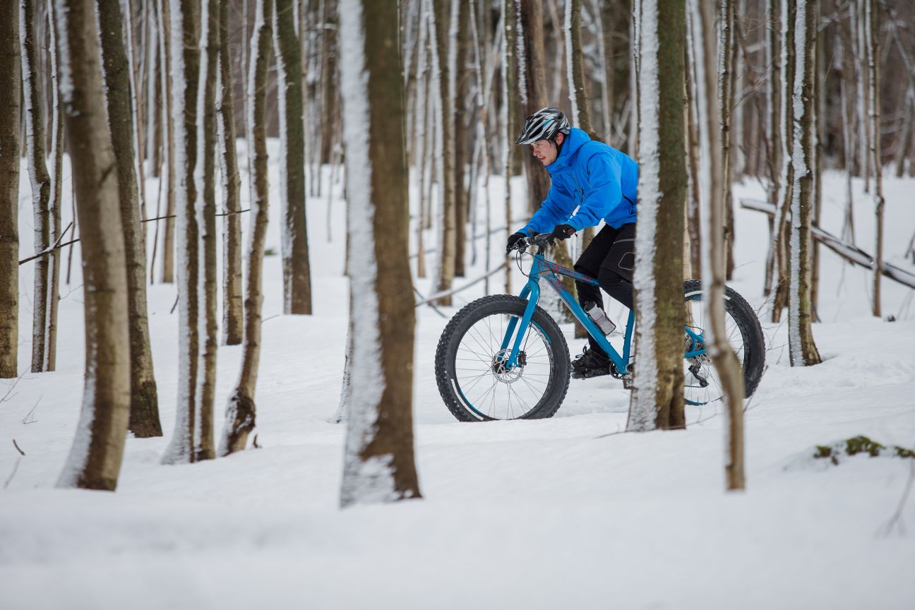 A fat biker rides through a snowy forest.