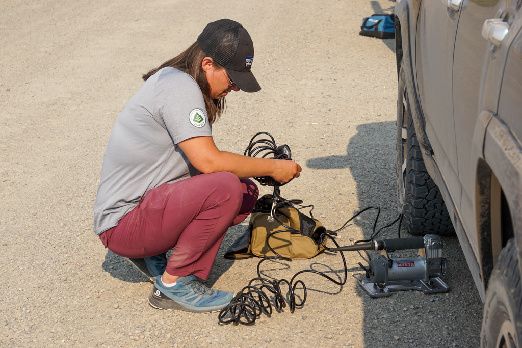 Person kneeling next to vehicle managing the air tubes for a compressor in order to put air back into the tires. 