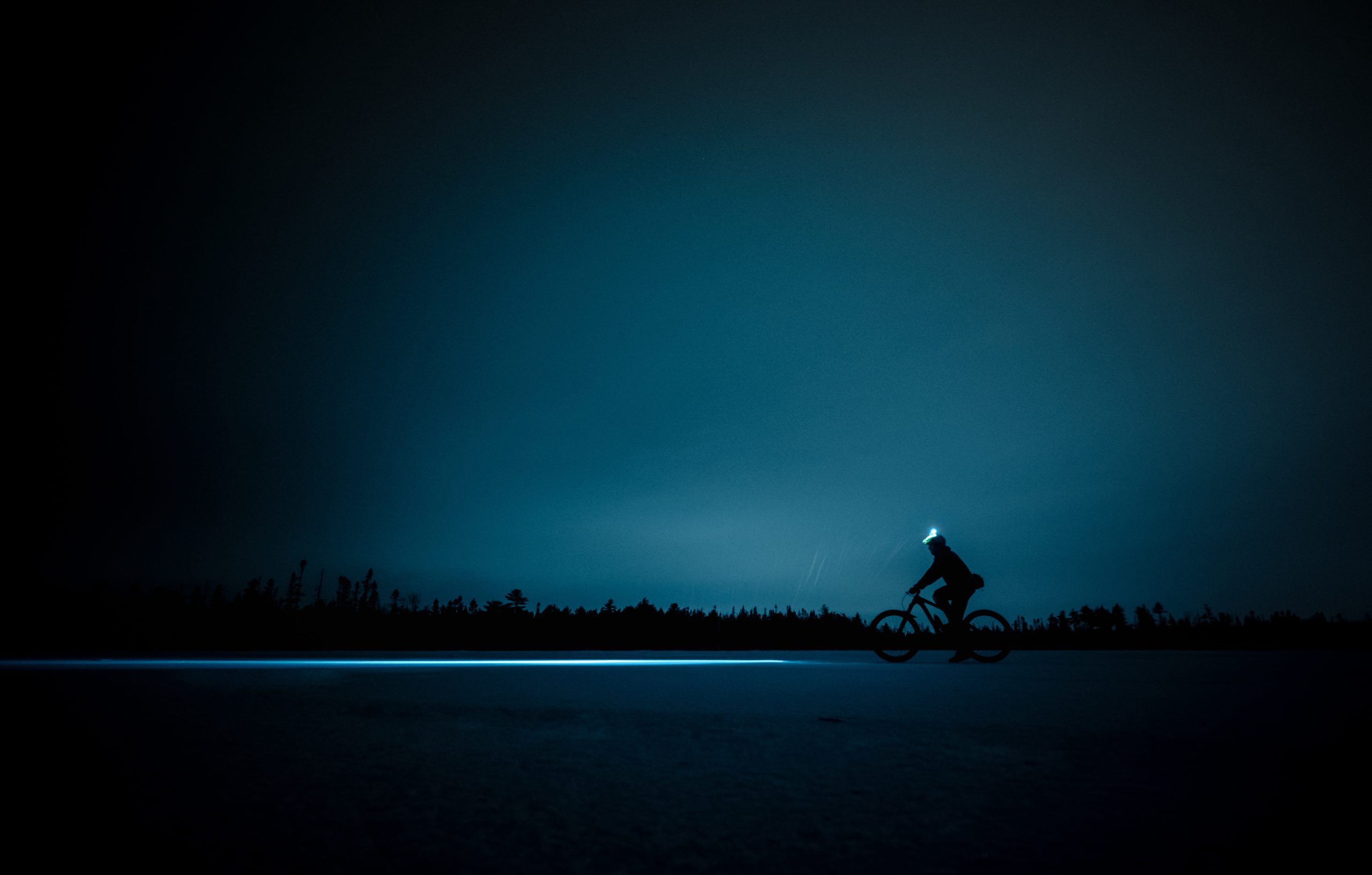 A fat biker rides over a snowy plain in the dark. 