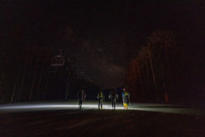 Four skiers skin up a mountain in the dark under the stars