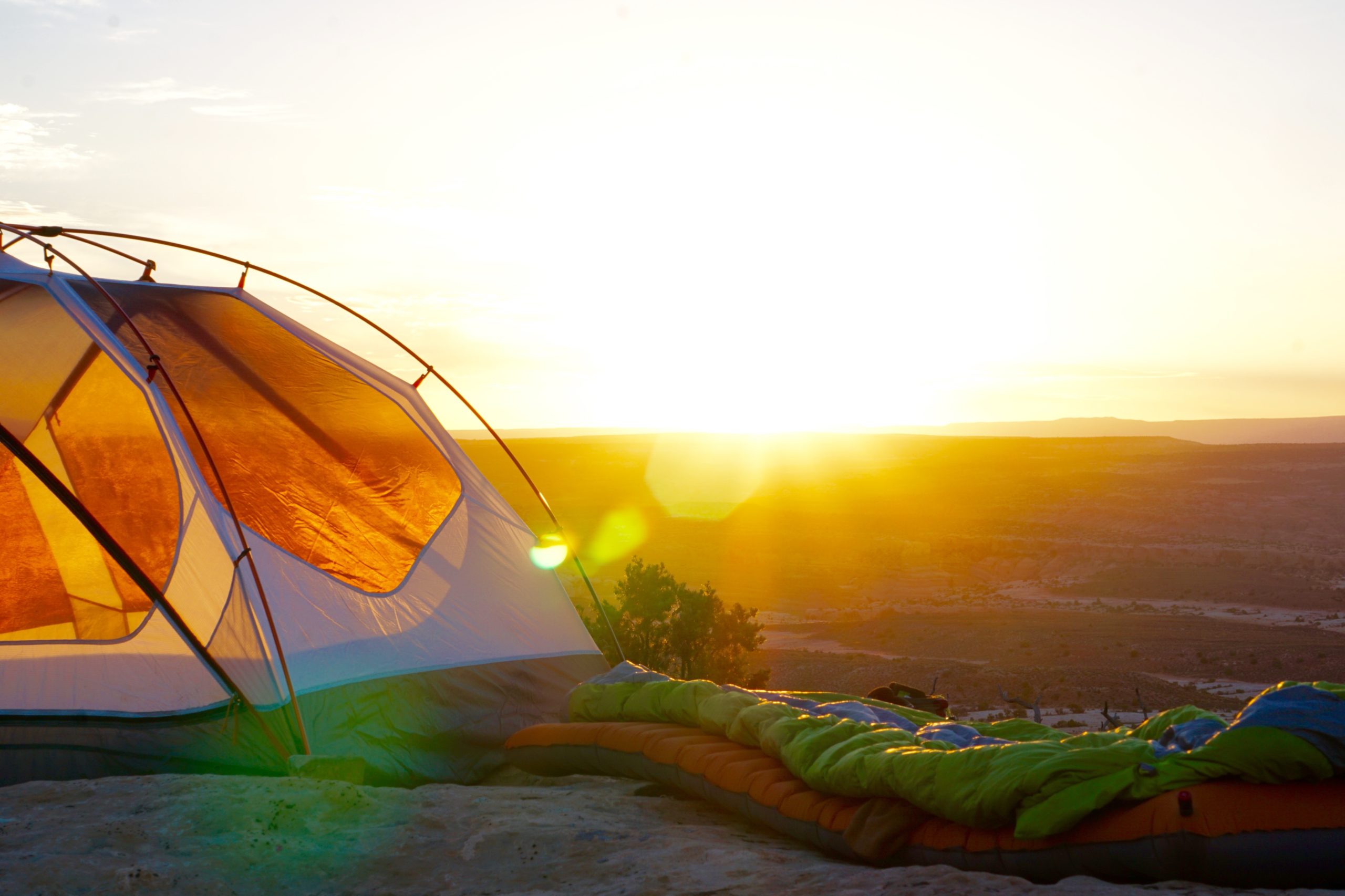 A tent with a sleeping bag and mat next to it in the desert.