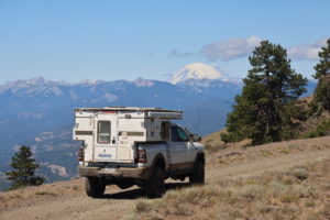 Overland rig drives on dirt road with mountains in the background.