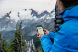 Someone holds their phone out infront of snow-capped mountains.