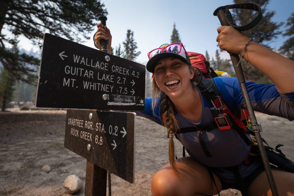 Allison smiles next to a trail sign on the JMT.