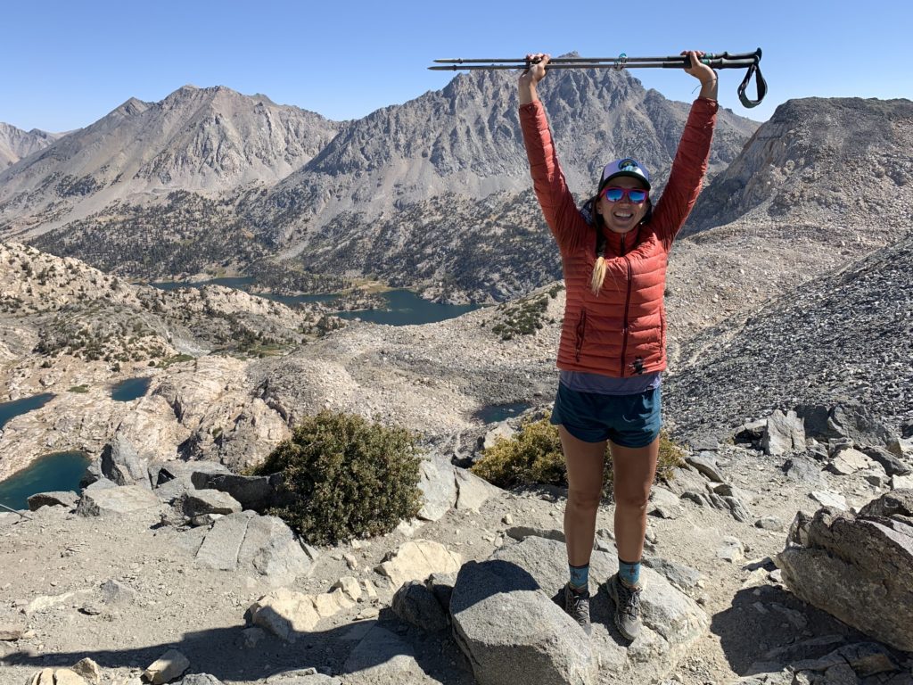 Allison smiles on the trail while holding her hiking poles over her head.