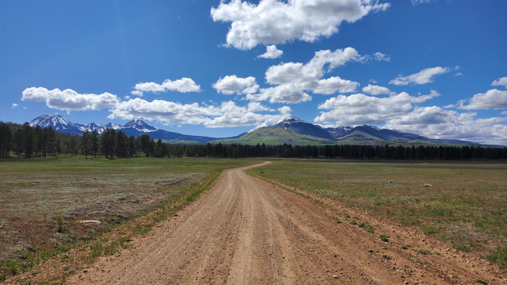 A view of a gravel road on the Rimrocker Trail in Colorado and Utah with blue sky and mountains in the background. 