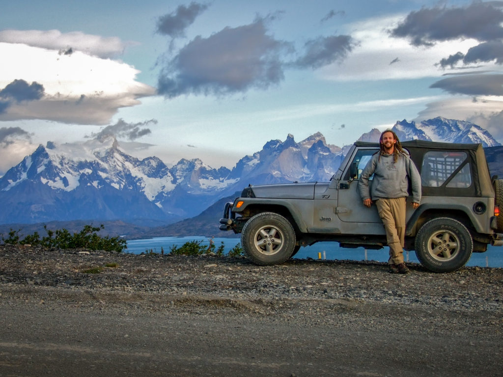 Grec in front of his Jeep with giant snow-capped peaks in the background.