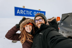 Richard and Ashley Giordano smiling in from of a road sign that says "Arctic Ocean"