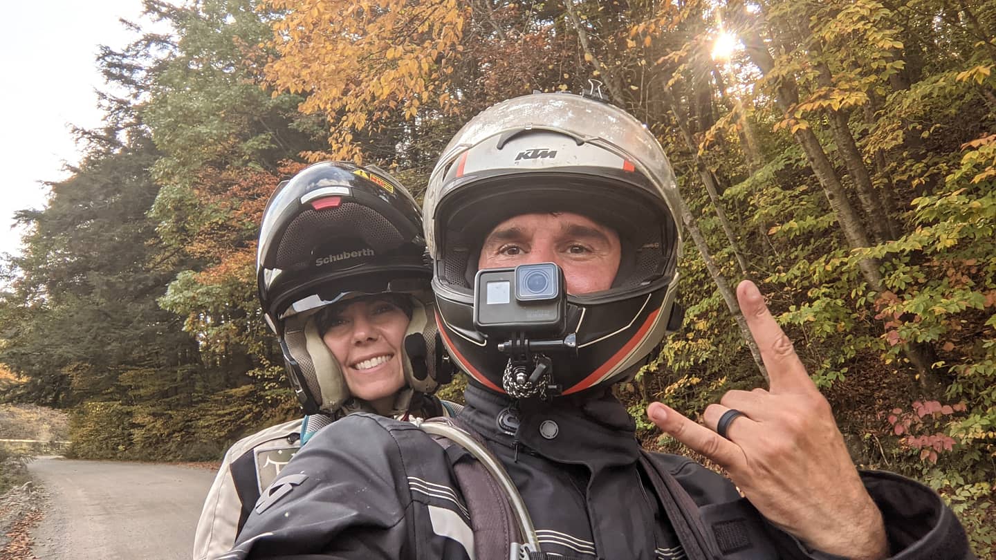 Tim and Marisa smile with their helmets on while riding their motorcycle. 