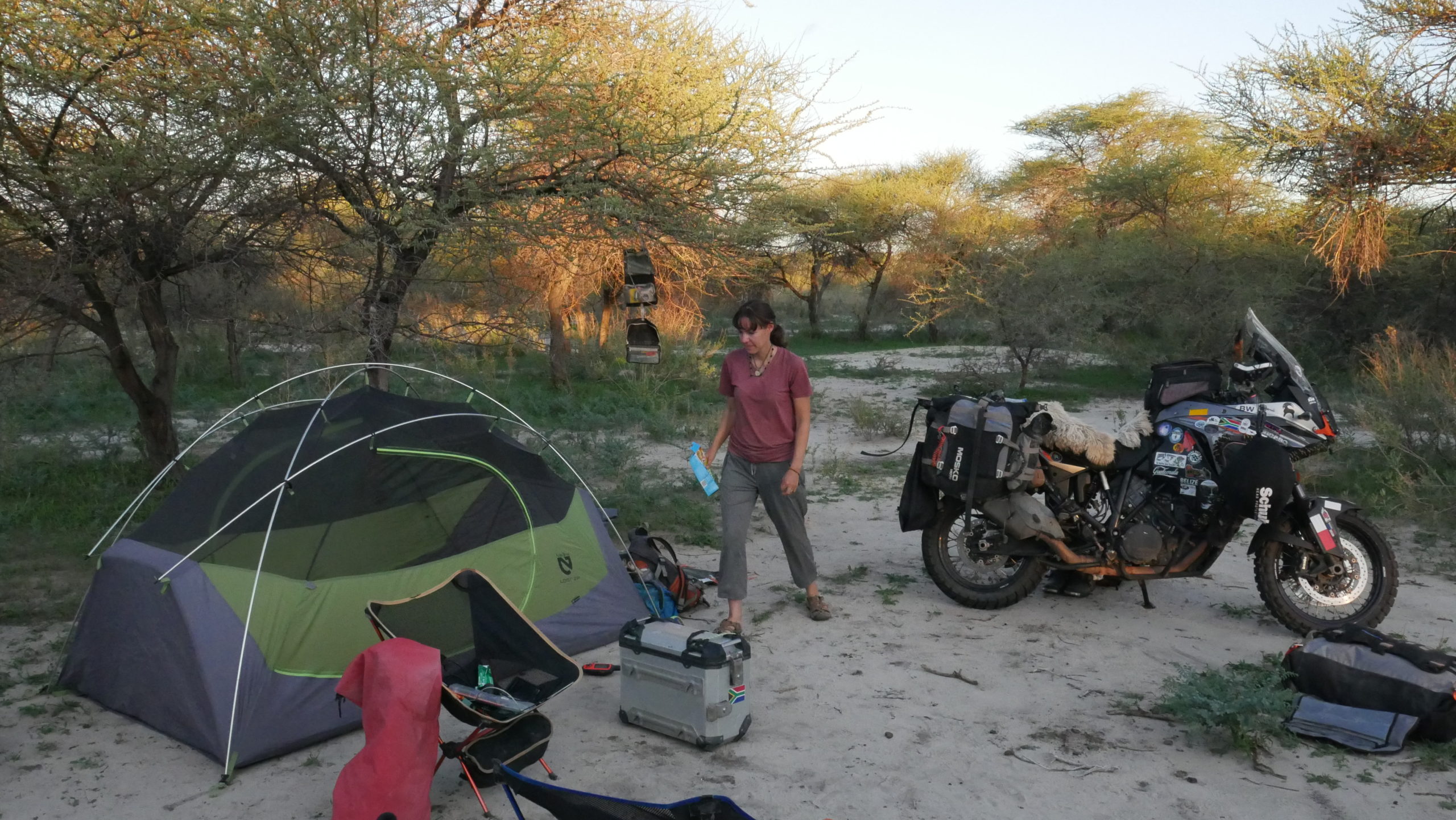 Marisa walks from a motorcycle parked in the sand to a tent set up nearby. 