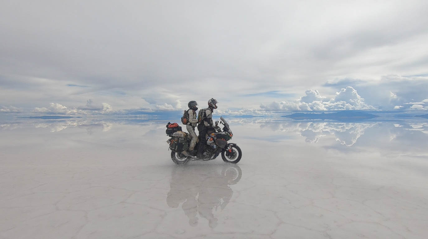 Tim and Marisa ride their motorcycle on a crystal clear lake.
