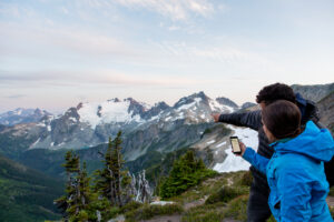 two people look at a phone while pointing to mountains in the distance.